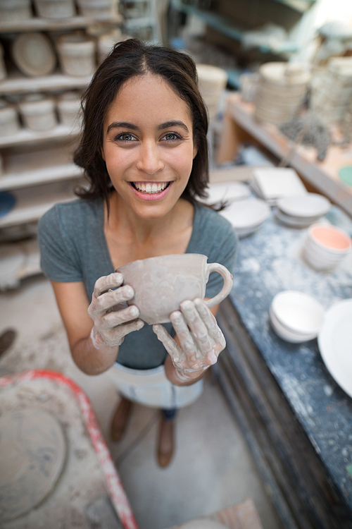 Portrait of female potter holding clay cup in pottery shop