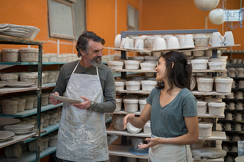 Male and female potter interacting with each other in pottery workshop