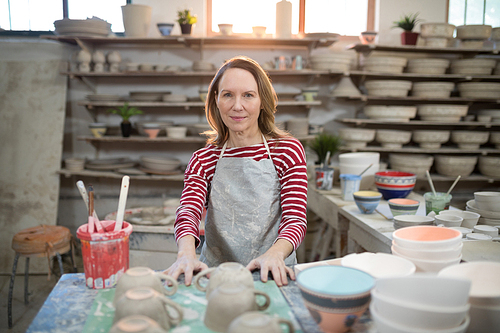 Portrait of female potter standing at worktop in pottery workshop