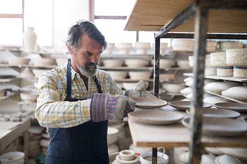 Male potter placing plate on shelf in pottery workshop