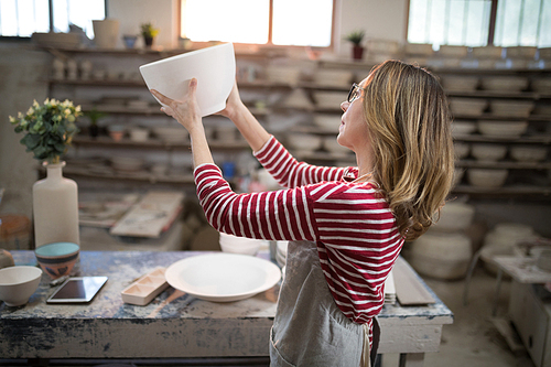 Female potter checking bowl in pottery workshop