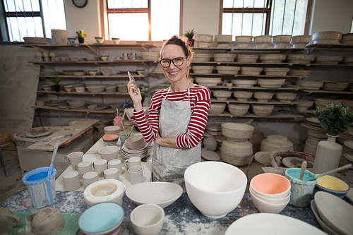 Portrait of female potter standing with mobile phone in pottery workshop