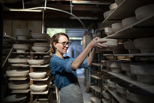 Female potter placing bowl in shelf at pottery workshop