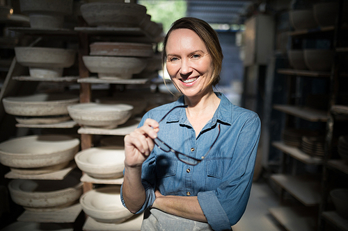 Portrait of female potter standing with spectacles in pottery workshop