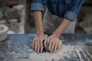 Mid section of female potter molding a clay in pottery shop