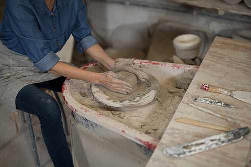 Mid section of female potter molding clay in pottery workshop