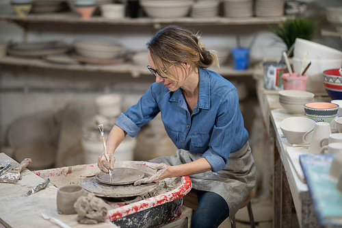 Female potter molding plate with hand tool in pottery workshop