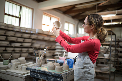 Woman checking mugs at worktop in pottery workshop