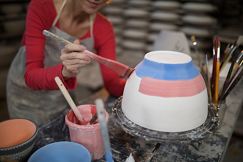 Mid section of female potter painting bowl in pottery workshop