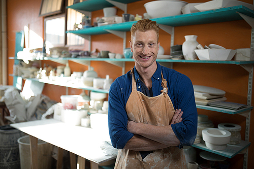 Portrait of male potter standing with arms crossed in pottery workshop