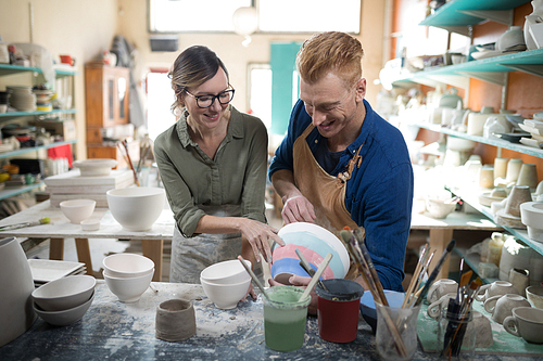 Male and female potter interacting with each other in pottery workshop