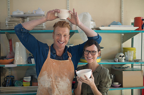 Portrait of male and female potter holding bowl in pottery workshop