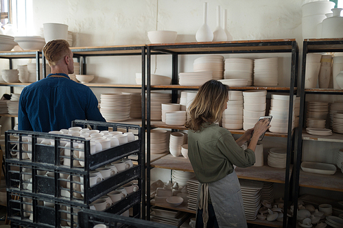 Male and female potter working maintaining records of earthenware in pottery workshop