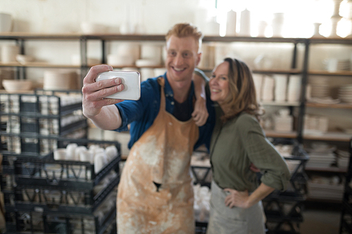 Male and female potter taking selfie with mobile phone in pottery workshop