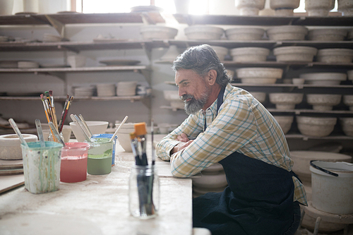 Thoughtful male potter sitting at worktop in pottery workshop