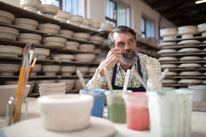 Thoughtful male potter sitting at worktop in pottery workshop