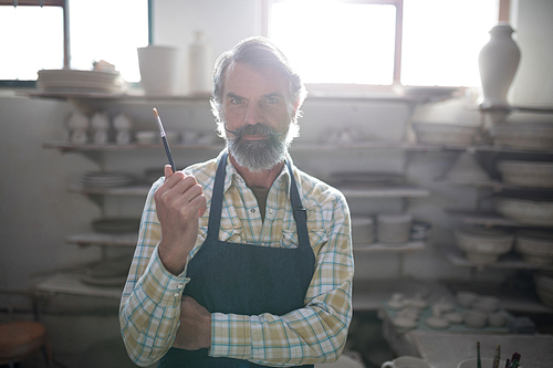 Portrait of male potter holding paint brush in pottery workshop