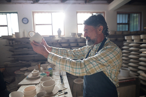 Male potter checking mug in pottery workshop