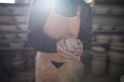 Mid section of male potter molding a clay in pottery workshop