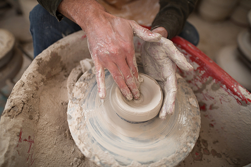 Mid section of male potter molding a clay in pottery workshop