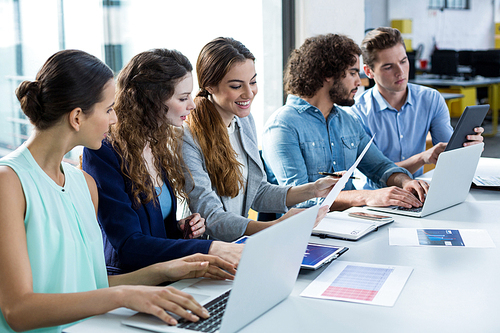 Smiling business team working on laptop and digital tablet in meeting at office