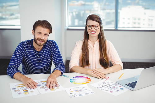 Portrait of smiling graphic designers sitting at desk in office