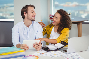 Smiling graphic designers sitting at table and using digital tablet in office