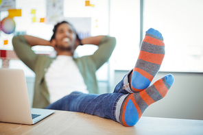 Male graphic designer relaxing with feet up at desk in office