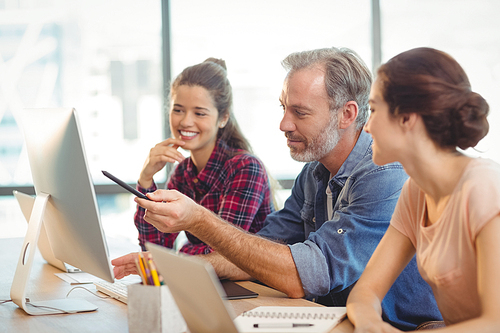 Team of graphic designers discussing over computer at desk in office