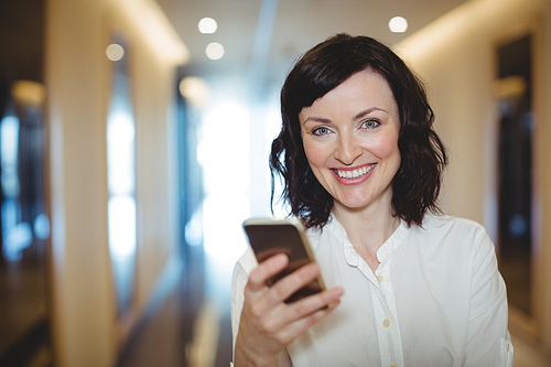 Portrait of female executive using mobile phone in corridor of office