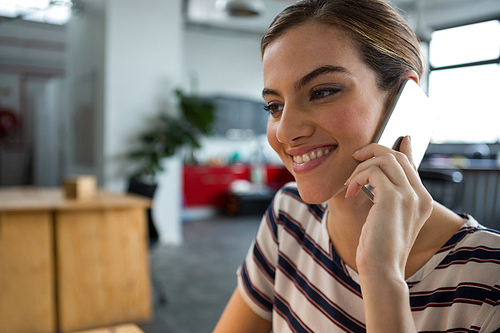 Smiling female graphic designer talking on mobile phone in creative office