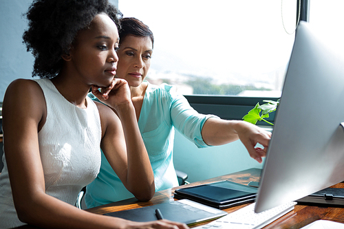 Female graphic designer pointing to desktop pc at creative office