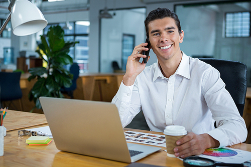 Happy man talking on mobile phone at desk in creative office