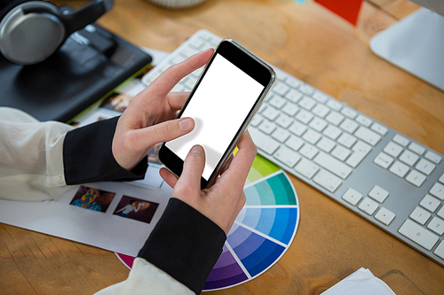 Close-up of female graphic designer using mobile phone at desk in office