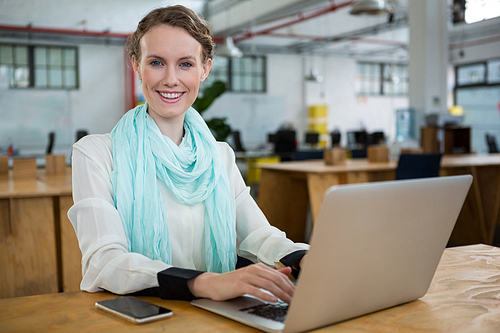 Portrait of female graphic designer using laptop at desk in creative office