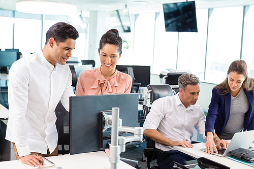 Smiling business colleagues interacting with each other at desk in office
