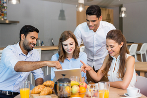 Business colleagues discussing over digital tablet while having breakfast in office cafeteria