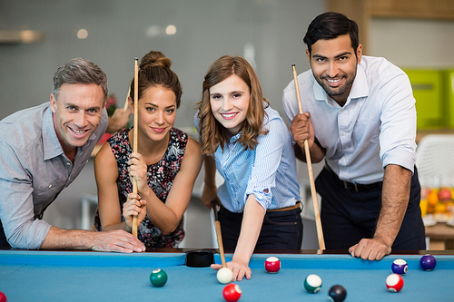 Portrait of smiling business colleagues playing pool in office space
