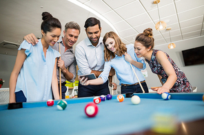 Smiling business colleagues using mobile phone while playing pool in office space