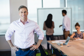 Portrait of smiling business executive standing with hands on hip in conference room at office