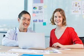 Smiling business colleagues discussing over laptop in conference room in office