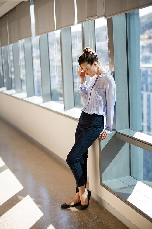 Tense female business executive leaning near window in office