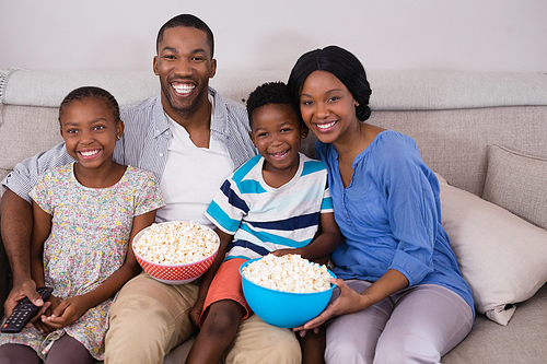 Cheerful family with popcorn bowls siting on sofa at home