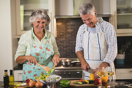 Portrait of smiling senior woman with man preparing food in kitchen at home