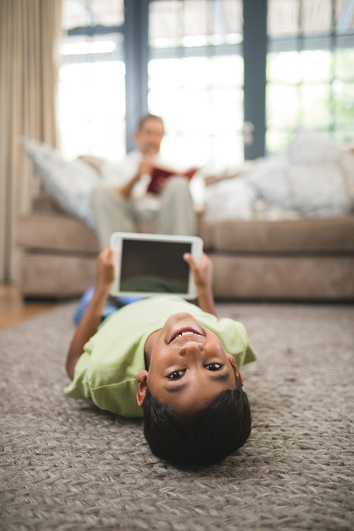 Portrait of smiling boy holding digital tablet while lying on carpet at home