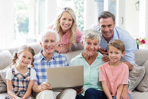 Portrait of happy multi-generation family with laptop in living room at home