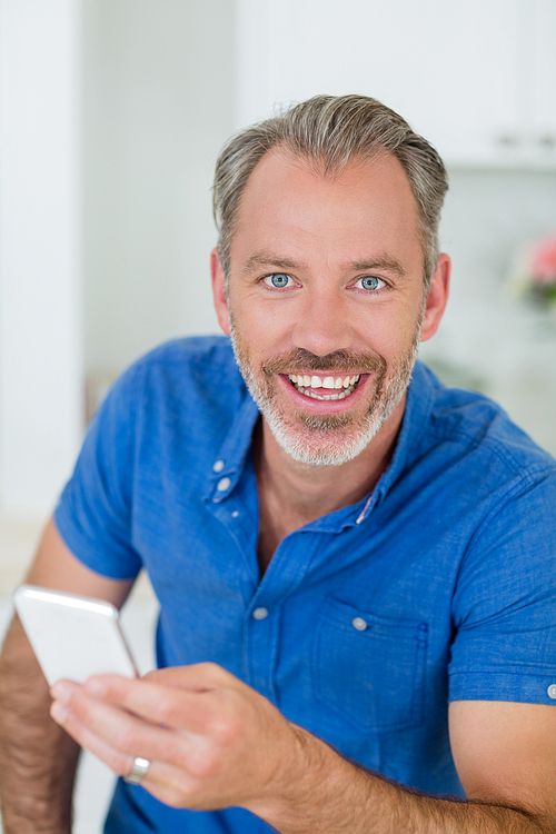 Portrait of smiling man holding mobile phone in kitchen at home