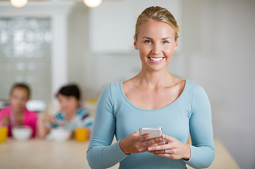 Portrait of happy beautiful woman using mobile phone in kitchen at home