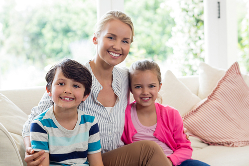 Portrait of smiling mother and kids relaxing on sofa in living room at home