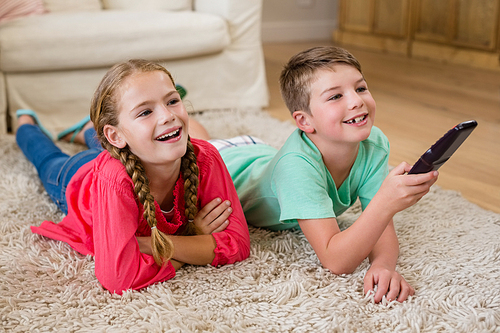 Siblings lying on rug and watching television in living room at home